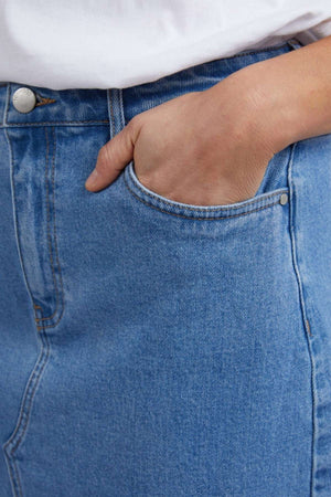 Close-up of someone in a fashion-forward midi skirt with a hand casually placed in the pocket. The vintage Foxwood Scout denim features visible stitching and a silver button, complemented by the glimpse of a white shirt at the top.