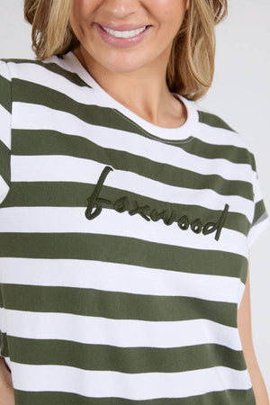 Woman smiling and wearing the Foxwood Signature Stripe Tee Dress—a white and olive green striped t-shirt dress with the Foxwood logo embroidered in black script across the chest.