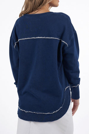 A woman is shown from the back wearing a dark blue Foxwood Simplified Crew sweater, featuring a relaxed fit with exposed seams and white distressed detailing, paired with a white skirt against a plain background.