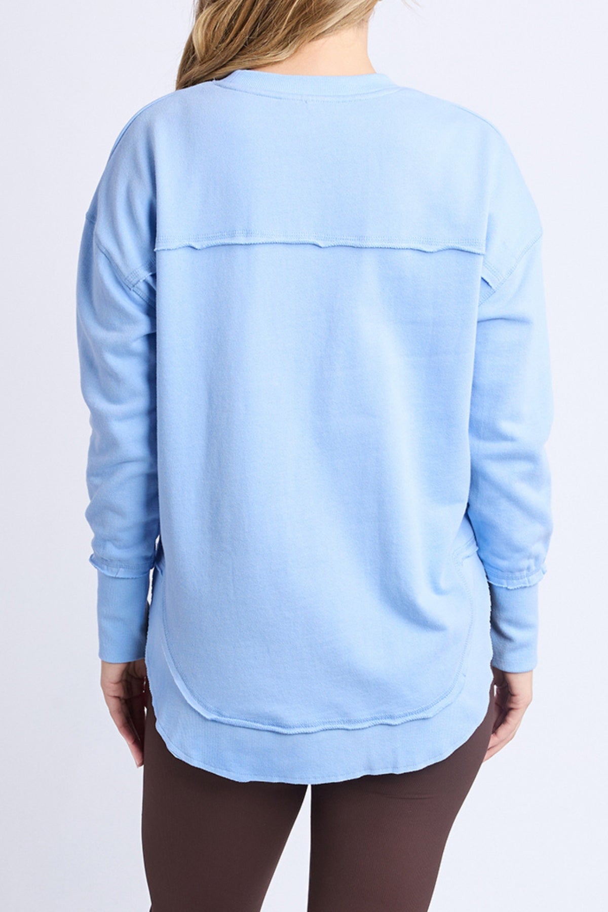A person with long, light hair is seen from the back wearing the loose-fitting Foxwood Simplified Metallic Crew women's sweatshirt with lurex thread, a horizontal seam, ribbed cuffs, and dark brown pants.