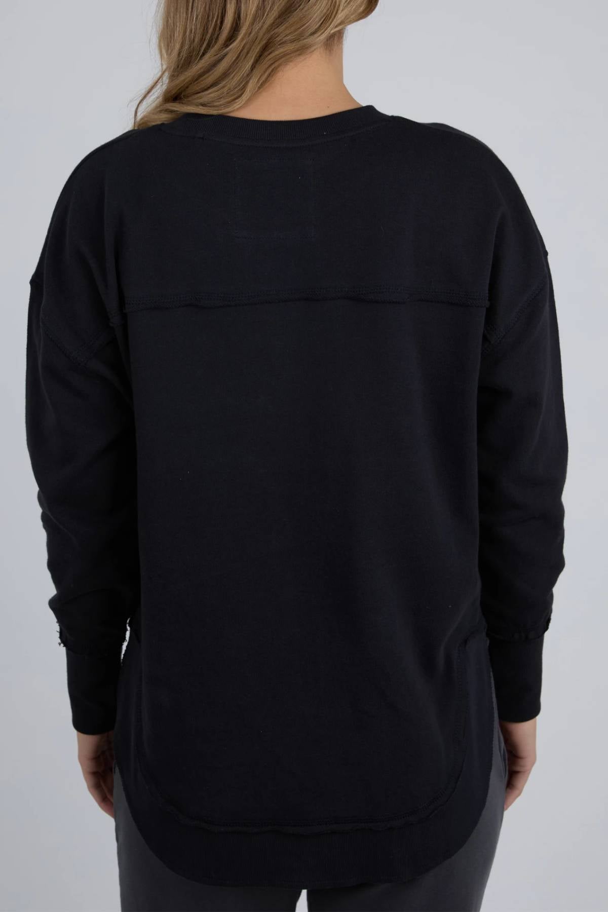 A person with long, light brown hair is seen from behind in the Foxwood Simplified Tonal Crew, a relaxed cotton fleece crew sweatshirt, paired with dark pants against a simple light gray background.
