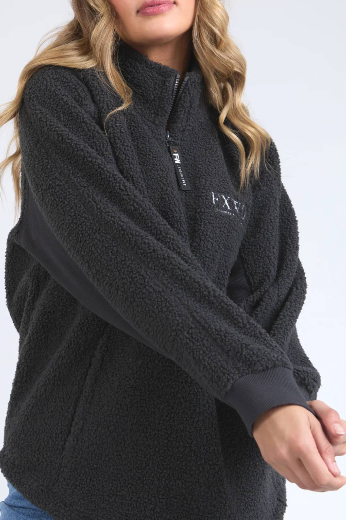 A woman with wavy blonde hair wears the black Foxwood Weekend Boucle Crew, standing with arms crossed against a plain light background. Her face is partially out of frame.