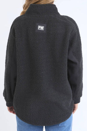 A person wears the black Foxwood Weekend Boucle Crew, featuring a textured finish and an FW logo patch on the upper back, styled with light blue jeans—ideal cozy loungewear for relaxing days—against a plain light background.