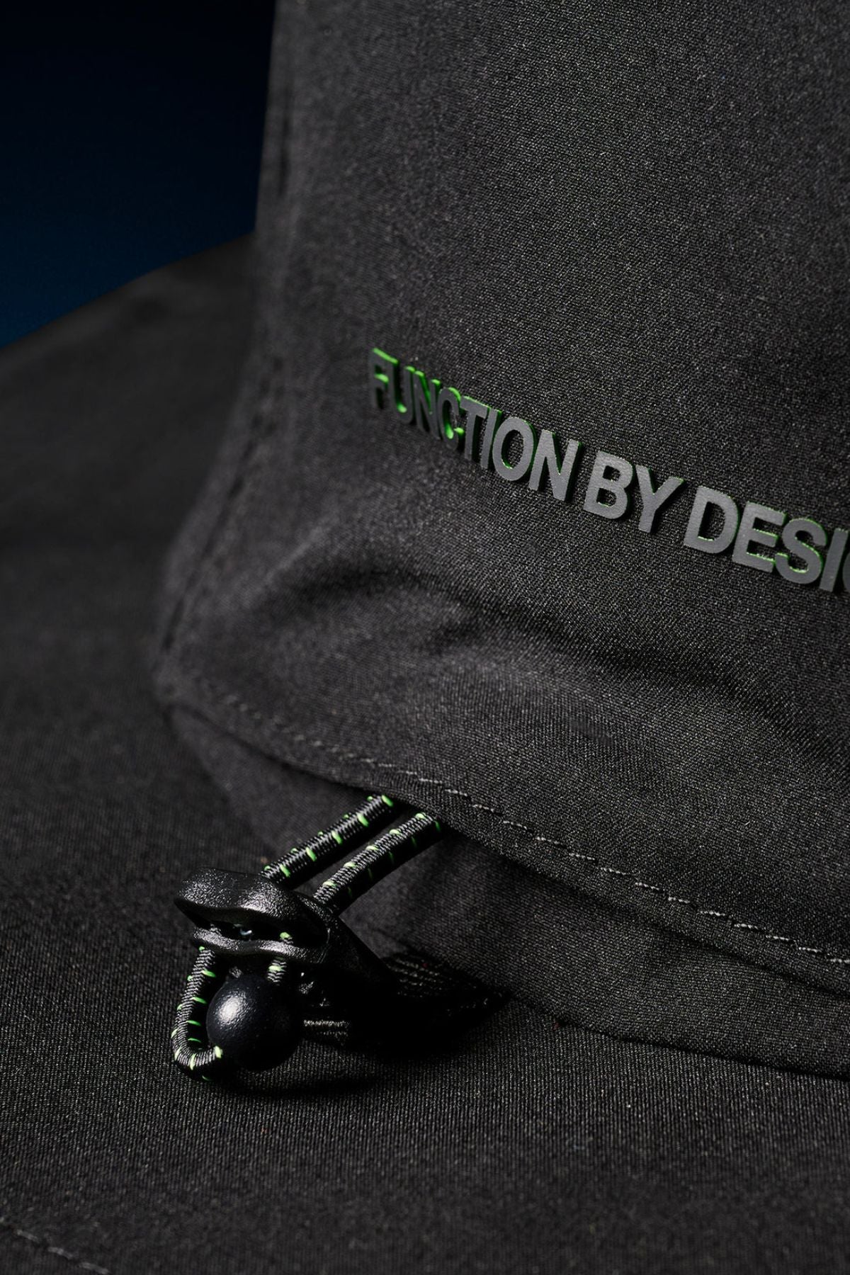 Close-up of the FXD CP-14 Boonie Hat in black, showing "FUNCTION BY DESIGN" text in green and white, plus an adjustable drawstring with toggle below—ideal for outdoor work and sun protection.