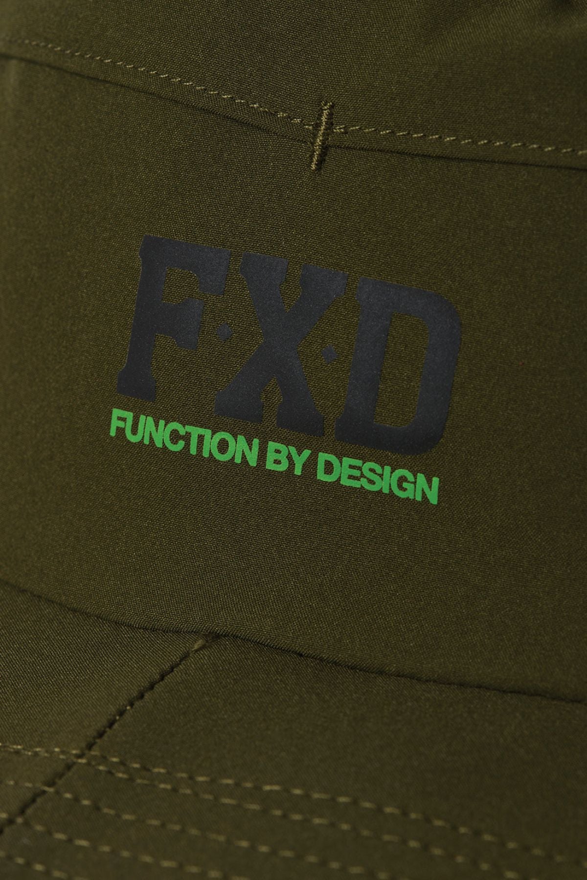 Close-up of olive green FXD CP-14 Boonie Hat fabric with "FXD" in black and "FUNCTION BY DESIGN" in green printed on it; visible seam stitching adds durability and sun protection for outdoor work.