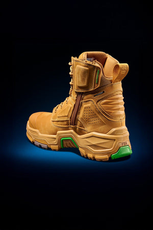 The FXD Dura X-1 Nitrocore™ High Cut Work Boots feature a tan design with rugged tread, green accents, reinforced heel, side zipper, and padded high ankle support, shown on a dark blue gradient background.