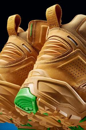 Close-up of the back and sole of two FXD Dura X-1 Nitrocore™ High Cut, High Performance Work Boots in tan with textured detailing and bright green outsole accents, set against a black background.