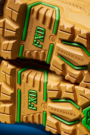 Close-up of the yellow and green treaded soles of FXD Dura X-1 Nitrocore™ High Cut, High Performance Work Boots, with "FXD," "NITROCORE," and "Oil, Heat, Slip Resistant" embossed on the bottom.