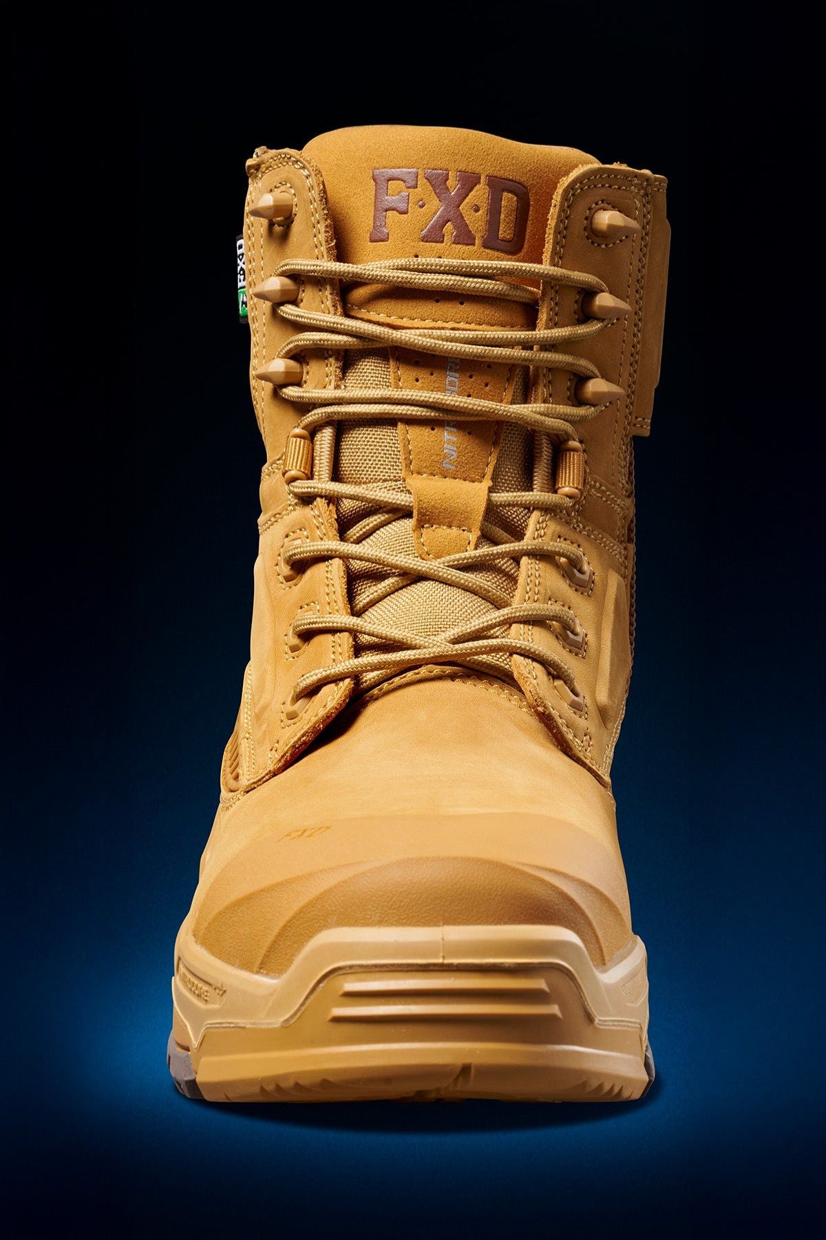 The FXD Dura X-1 Nitrocore™ High Cut Work Boot, tan with laces and visible stitching, is shown from the front against a dark blue gradient. "FXD" is printed on the tongue.