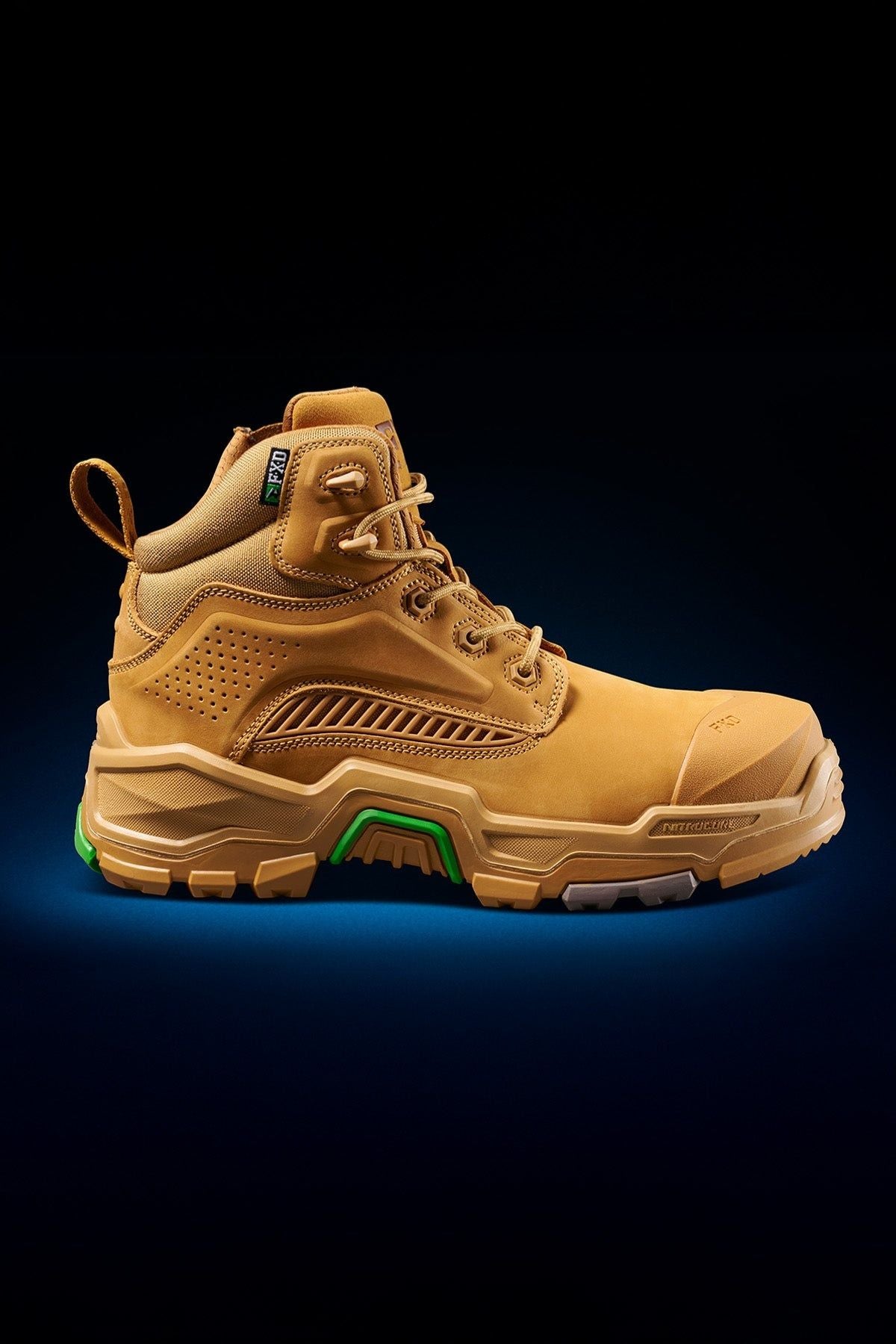 The FXD Dura X-2 Nitrocore™ Mid Cut High Performance Work Boot features a tan upper, rugged sole, green accents on the heel and midsole, and detailed stitching, shown on a dark gradient background.