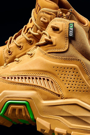 Close-up of FXD Dura X-2 Nitrocore™ Mid Cut High Performance Work Boots featuring tan textured leather, green sole accents, detailed stitching, perforated side panels, and sturdy laces against a black background.