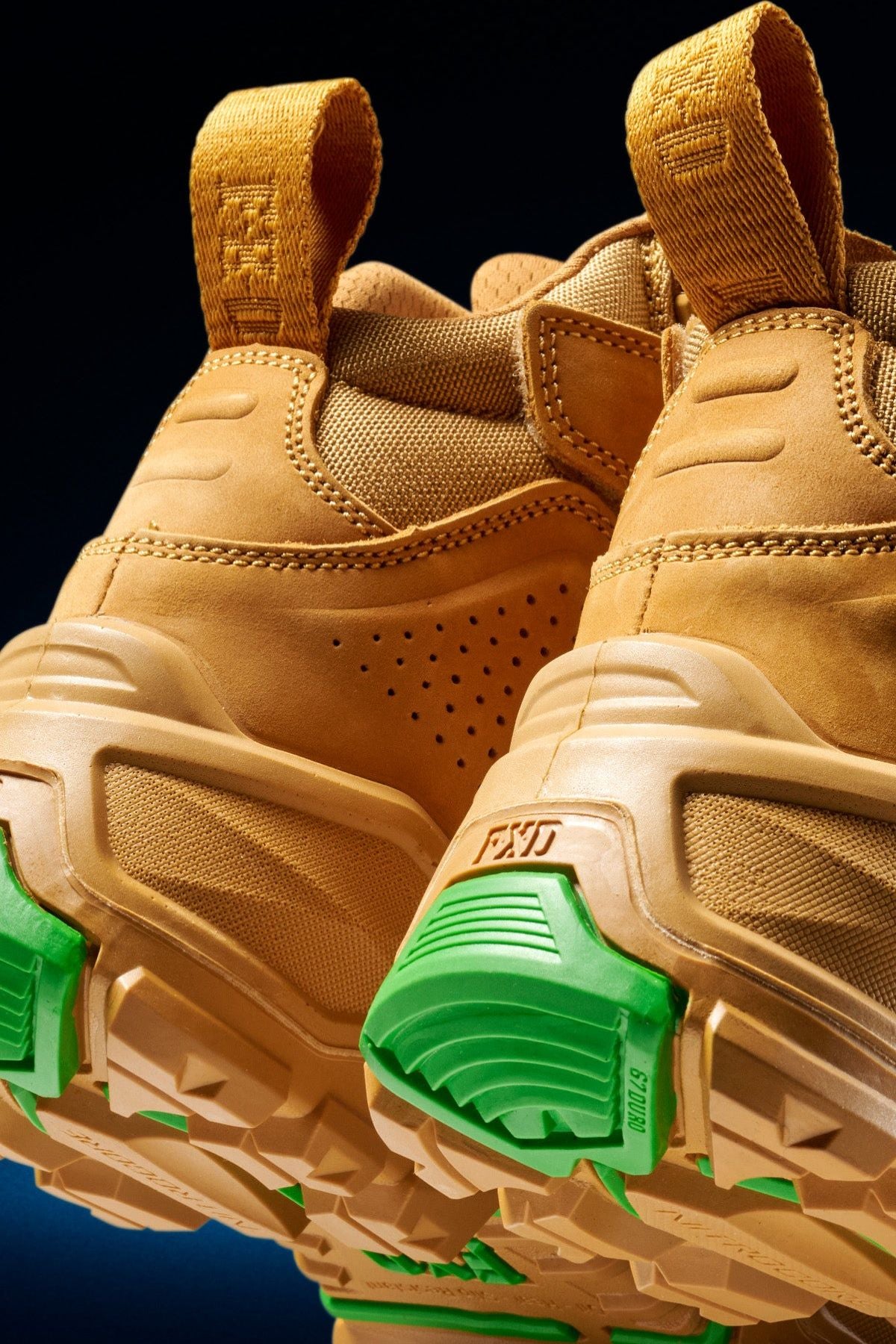 Close-up of the back and soles of FXD Dura X-2 Nitrocore™ Mid Cut High Performance Work Boots, featuring textured beige uppers, yellow pull tabs, chunky tan outsoles, and bright green accents on the heel and tread.