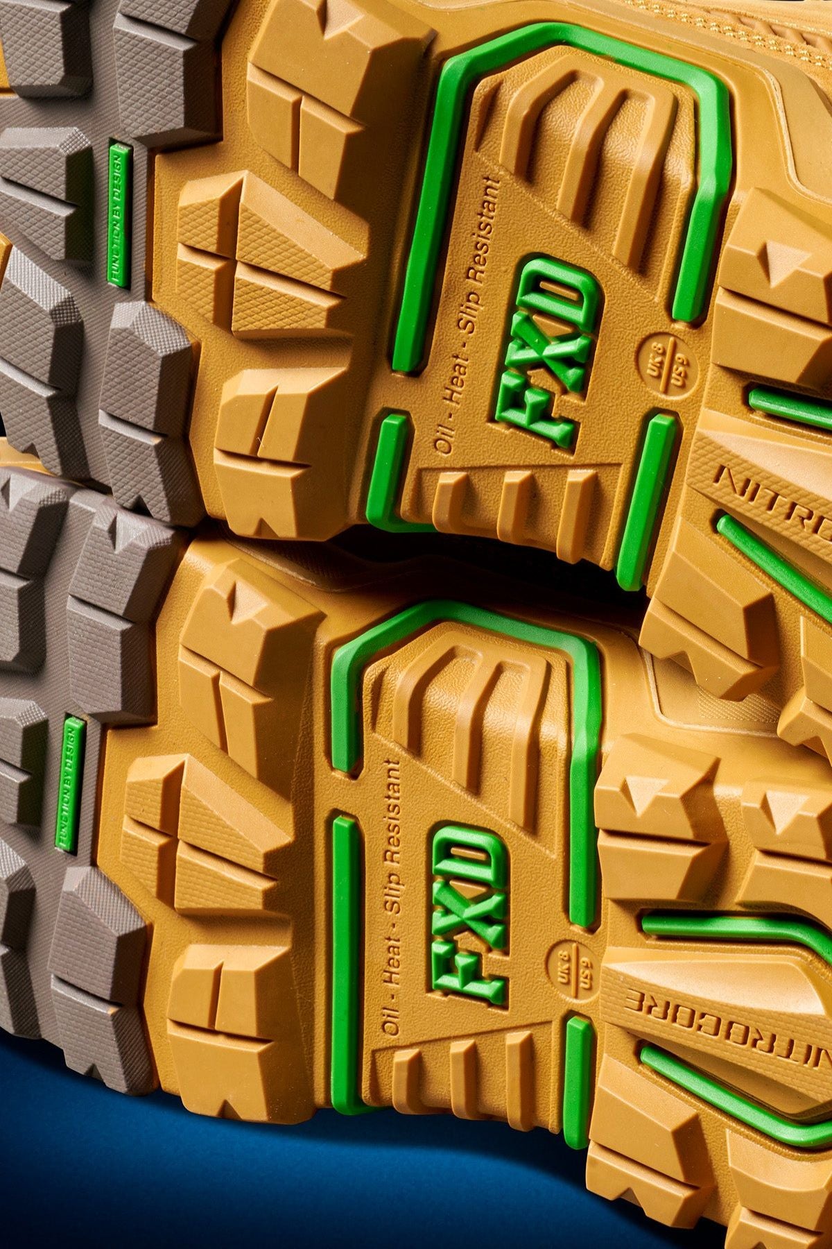 Close-up of the yellow and green treaded soles on FXD Dura X-2 Nitrocore™ Mid Cut, High Performance Work Boots, featuring bold branding and "Oil, Heat, Slip Resistant" text on a blue background.