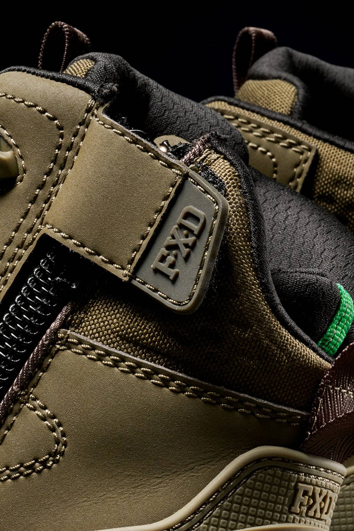 Close-up of the FXD WB-6 Work Boot, featuring a rugged olive-green design with brown and black accents, visible stitching, a synthetic upper, side zipper, and an "FXD" tag near the ankle.