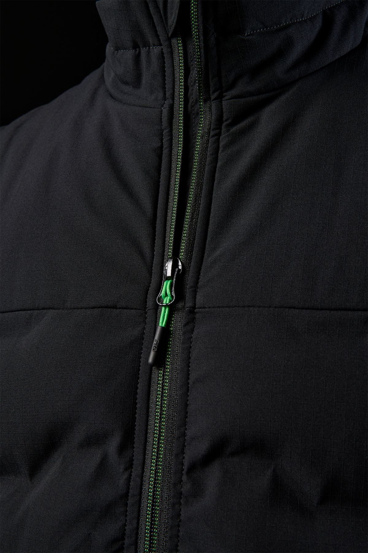 Close-up of the FXD WO-6 Insulated Puffer Vest showing its green and black zipper, vertical stitch lines, and padded performance fabric that highlights the texture and details of the front.