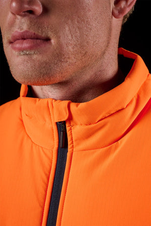 Close-up of a person wearing the FXD WO-6 Hi Vis Insulated Puffer Vest in bright orange, featuring a high collar and black zipper. Only their lower face with stubble is visible against a dark background.