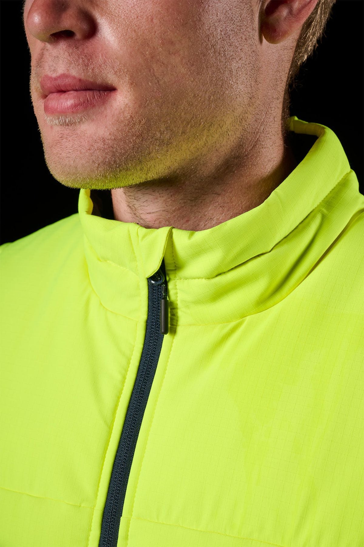 Close-up of a person wearing the FXD WO-6 Hi Vis Insulated Puffer Vest with a high collar. Only the lower half of the face is visible, set against a black background.