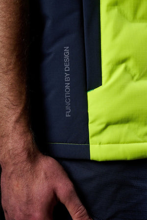 A close-up of a hand next to the FXD WO-6 Hi Vis Insulated Puffer Vest, featuring black and bright yellow-green panels with "FUNCTION BY DESIGN" printed vertically on the black panel.