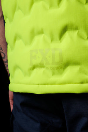 Close-up of a person wearing the FXD WO-6 Hi Vis Insulated Puffer Vest in bright yellow, with "FXD" and "Function by Design" embossed on it, paired with dark pants. A portion of their tattooed arm is visible.