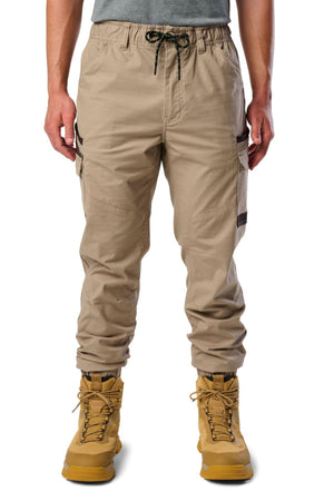 Someone stands against a white background wearing beige FXD WP-12C stretch ripstop work pants with black drawstrings and side pockets, paired with a gray shirt and tan lace-up boots.