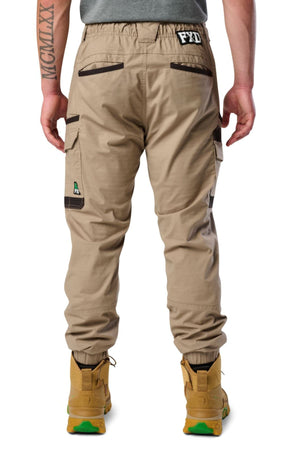 Seen from behind, a person wears FXD WP-12C stretch ripstop utility pants with black accents, multiple pockets, a right leg patch, tan boots, and has a tattoo on their left forearm.