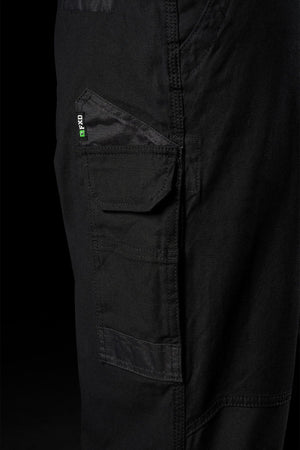 Close-up of black FXD WP-3L Loose Fit Stretch Canvas Work Pants featuring a side pocket with a small green and white label, set against a dark background.