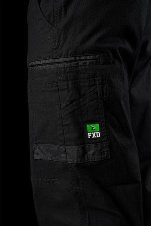 Close-up of a black FXD WP-3L Loose Fit Stretch Canvas Work Pants pocket with a small green and black FXD brand label, set against a black background.