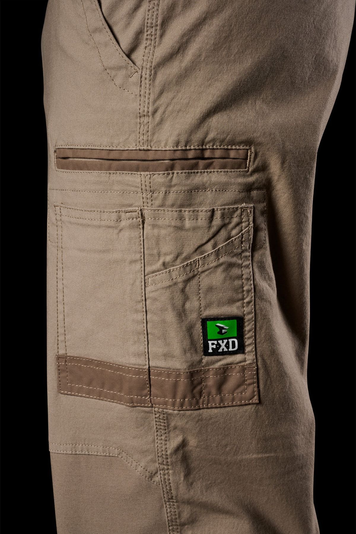 Close-up of FXD WP-3L Loose Fit Stretch Canvas Work Pants in tan, showcasing multiple pockets, visible stitching, and a green and black FXD logo tag on the pocket.