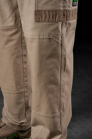 Close-up of a person wearing FXD WP-3L Loose Fit Stretch Canvas Work Pants in light brown with brown shoes featuring green accents, standing on a dark textured floor—showcasing the pants' durable fabric and detailed stitching.