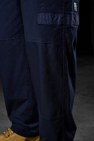 Close-up of a person wearing FXD WP-3L Loose Fit Stretch Canvas Work Pants in navy blue, featuring visible pockets and stitching. Only the lower legs and tan shoes are visible as they stand on a concrete floor.