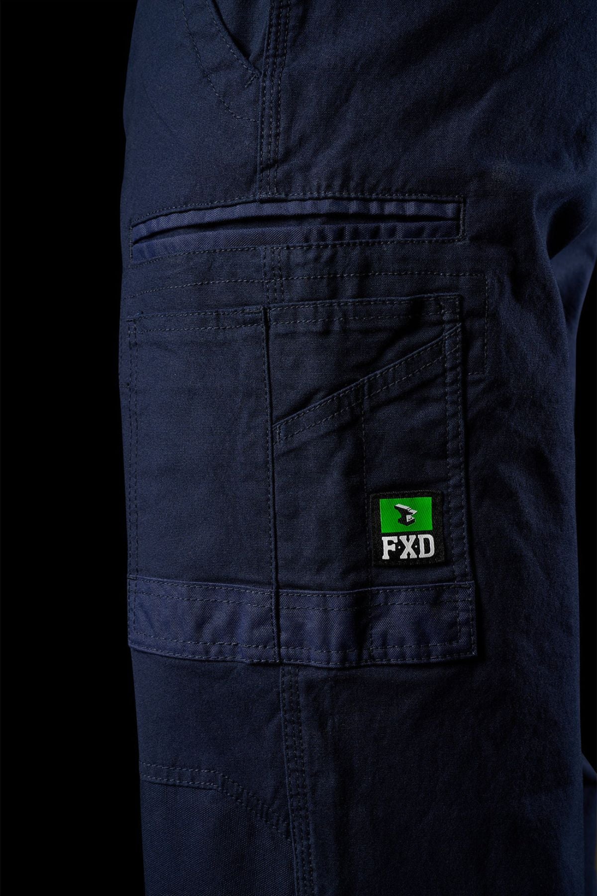Close-up of the side pocket detail on FXD WP-3L Loose Fit Stretch Canvas Work Pants in navy, showing visible stitching and a green/black FXD logo patch. These stretch pants offer comfort and durability.