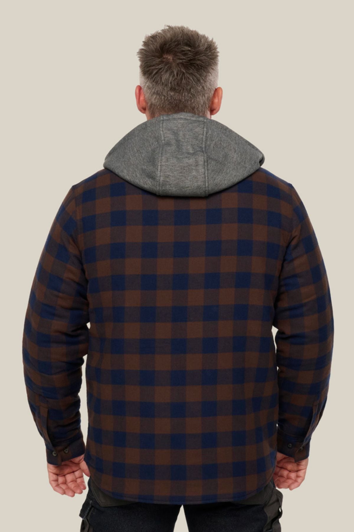A man faces away from the camera, wearing a Hard Yakka Quilted Flannelette Shacket in brown and navy check with a gray hood, set against a plain light beige background.