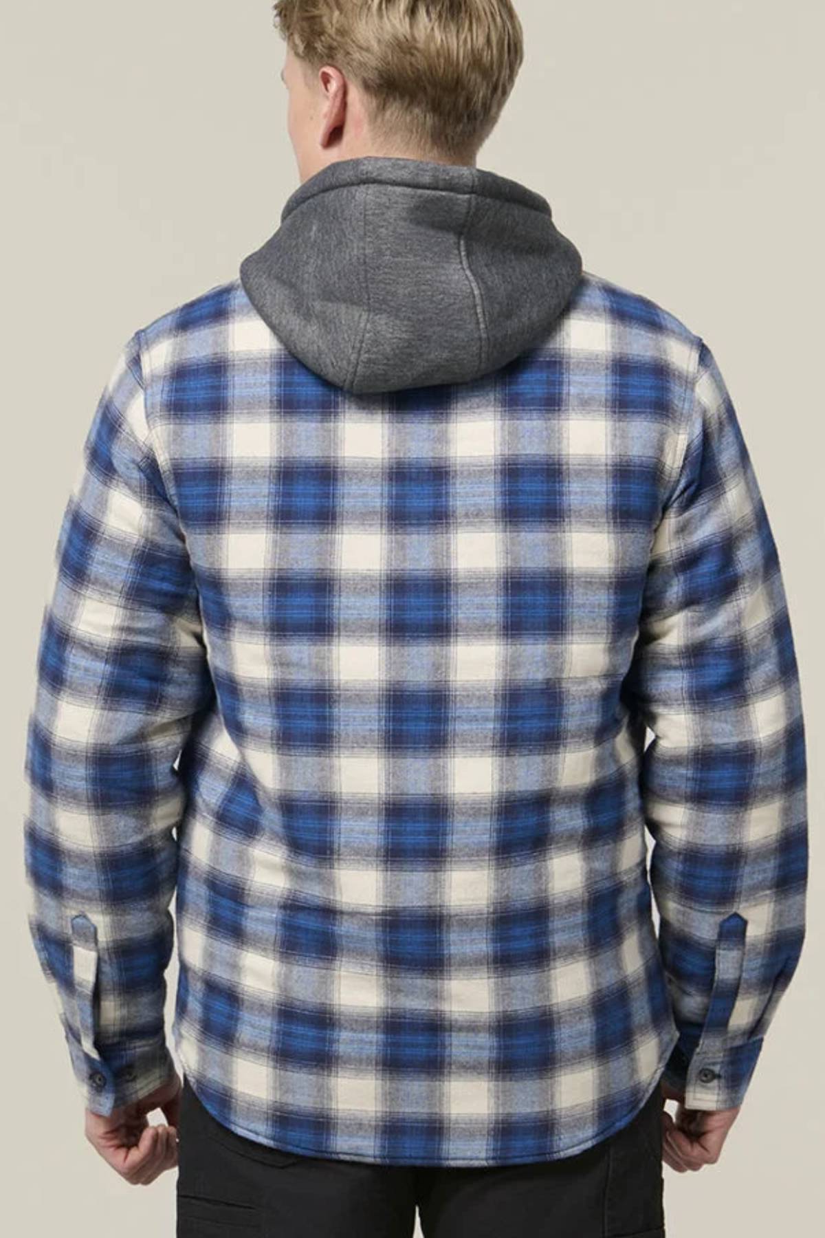 A person facing away from the camera wears a blue and white plaid Hard Yakka Quilted Flannelette Shacket with a gray hood and black pants, standing against a plain light background.