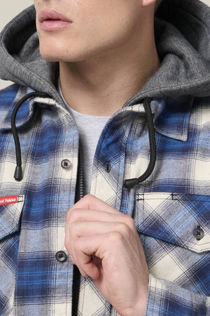 A person in a blue and white Hard Yakka Quilted Flannelette Shacket with a gray hood holds the jacket closed; only the lower half of their face is visible.