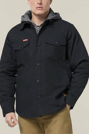 A person in a black Hard Yakka Quilted Solid Shacket with chest pockets, layered over a gray hoodie and tan pants, stands against a plain light background.