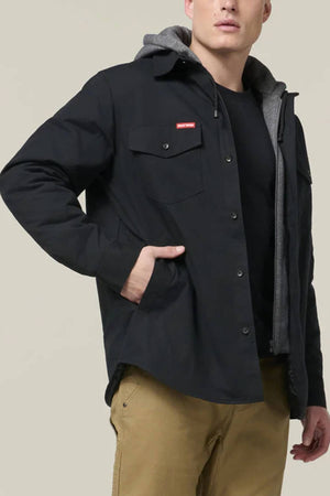 Wearing the Hard Yakka Quilted Solid Shacket in black over a grey hoodie, black tee, and tan pants, a person stands with one hand in their pocket against a plain light background.