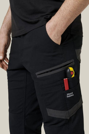 Someone stands with one hand in their pocket, wearing Hard Yakka Raptor Pant; scissors and a pen are visible in the side pocket.