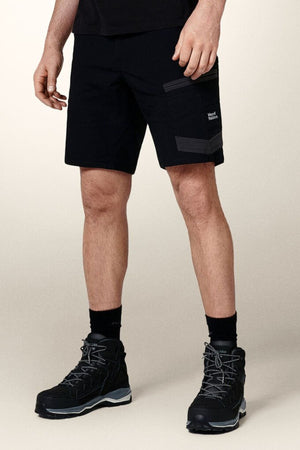 Someone is wearing black Hard Yakka Raptor Mid Shorts with an Active Fit stretch waistband and black hiking boots. Featuring a small "Wood Wood" logo on the left side, the shorts stand out against the plain, light-colored background, emphasizing both practicality and style.