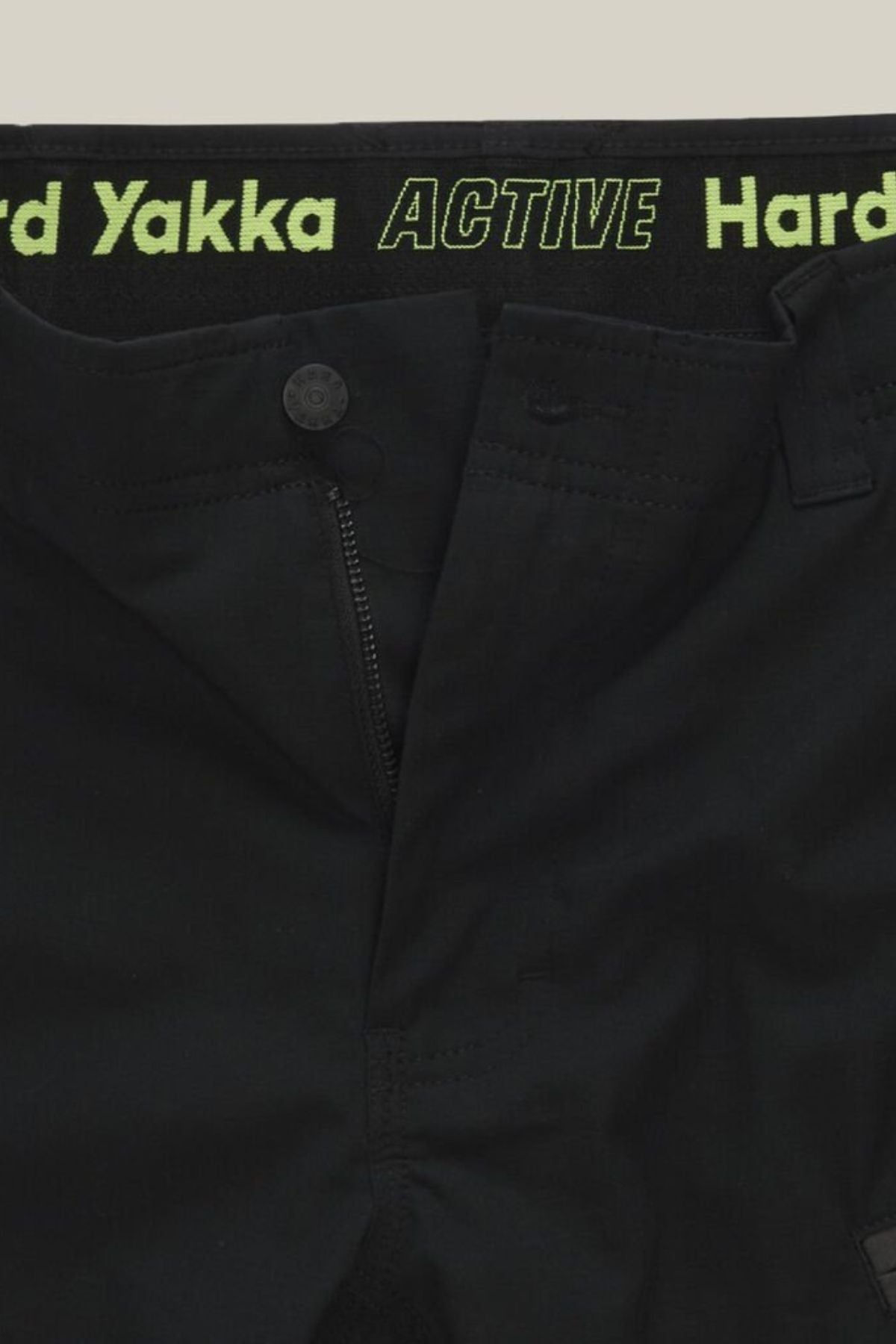 Close-up of Hard Yakka Raptor Mid Shorts with a partially open zipper, displaying "Hard Yakka ACTIVE" in green on the Active Fit stretch waistband and featuring a button closure above the zipper.