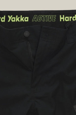 Close-up of Hard Yakka Raptor Mid Shorts with a partially open zipper, displaying "Hard Yakka ACTIVE" in green on the Active Fit stretch waistband and featuring a button closure above the zipper.