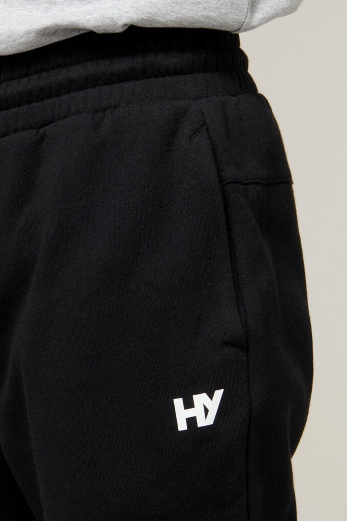 Close-up of a person wearing Hard Yakka Xtreme Joggers, featuring a white "HY" logo on the right hip, symbolizing Hard Yakka. The person pairs them with a grey top, and the image spotlights the side profile of the joggers, highlighting reinforced knee patches for enhanced durability.
