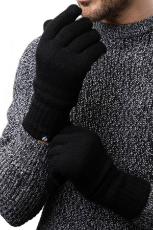 A person in a chunky gray knit sweater adjusts one black Heat Holders Oslo Mens Thermal Glove with the other hand. Only the lower half of their face and upper body are visible in the photo.