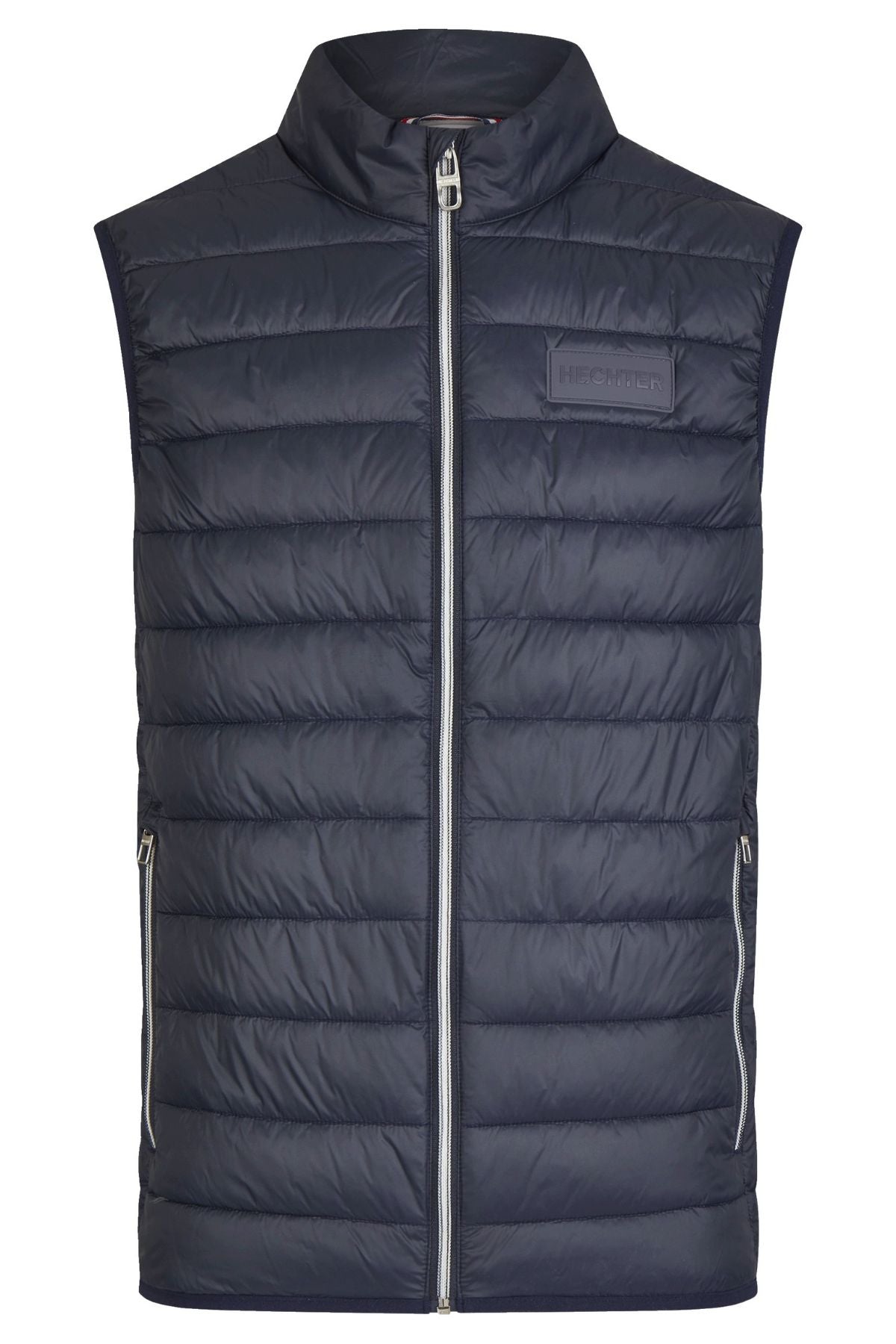 The Hechter Puffer Vest is navy blue and sleeveless, with horizontal quilting, a high collar, full front zipper, zippered side pockets, and a small rubber logo patch on the left chest.