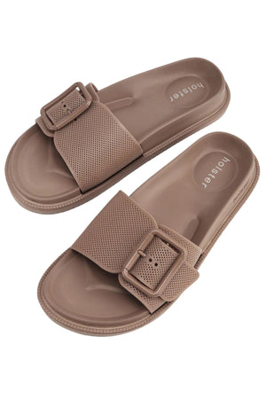 A pair of Holster Laze light brown vegan sandals featuring textured, perforated straps and large rectangular buckles, displayed on a white background. "honeyer" is printed on the footbed.