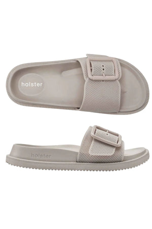 Two views of the Holster Laze slide sandal in light beige, featuring a large textured strap with adjustable buckle, contoured footbed with arch support, and visible "holster" branding. Top view shows the shape; side view displays strap and sole details.