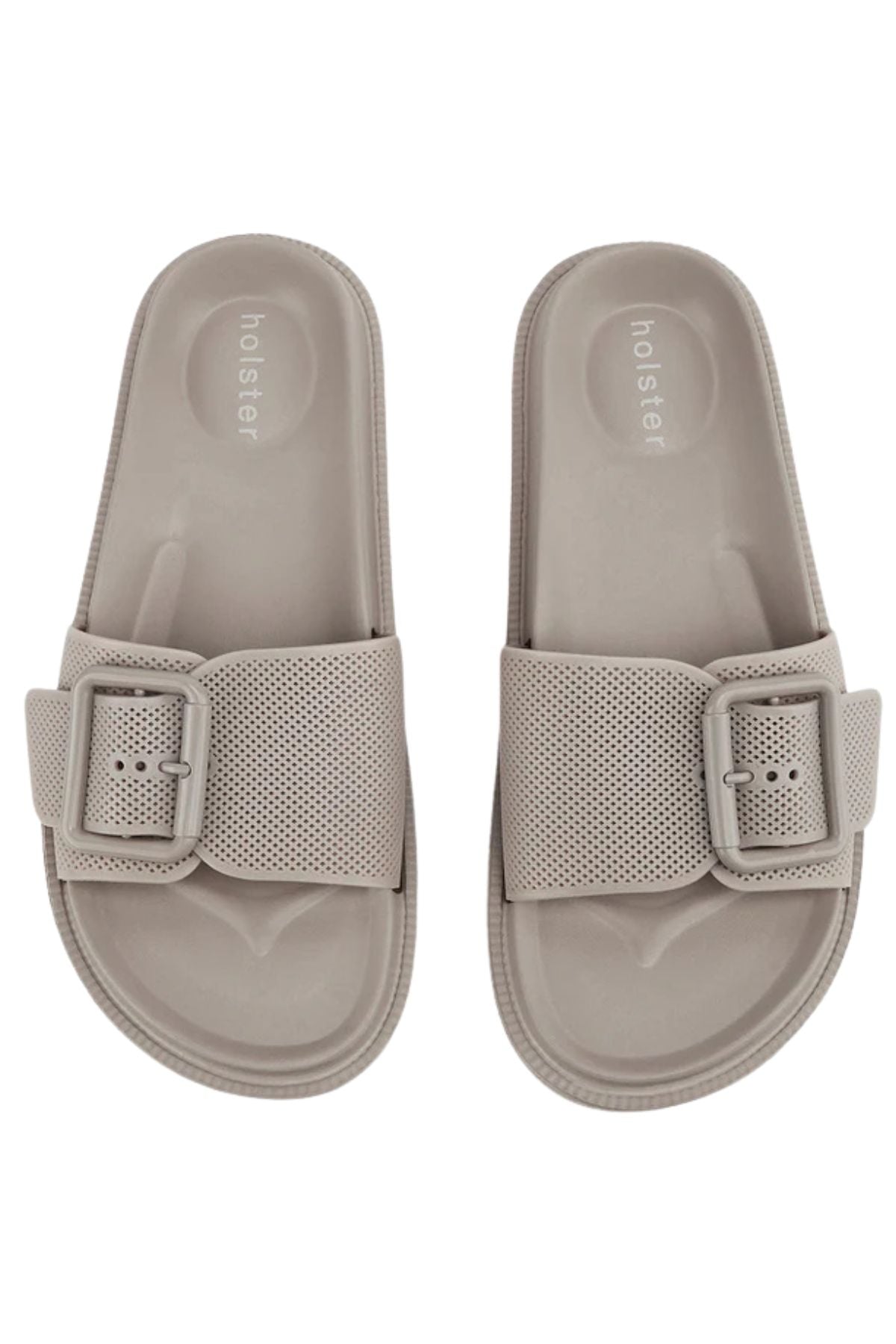 The Holster Laze sandals are light beige vegan slides with wide perforated straps, large buckles, and "holster" printed on the insole, shown from above.