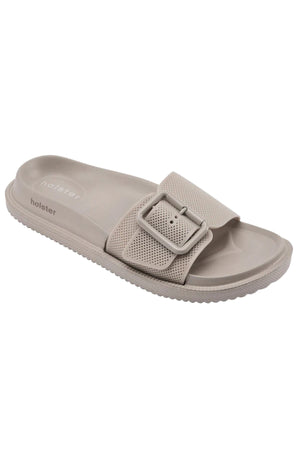 The Holster Laze is a beige vegan slide sandal featuring a textured sole, perforated wide strap, large matching buckle, and "holster" embossed on the footbed—designed for comfort and style.