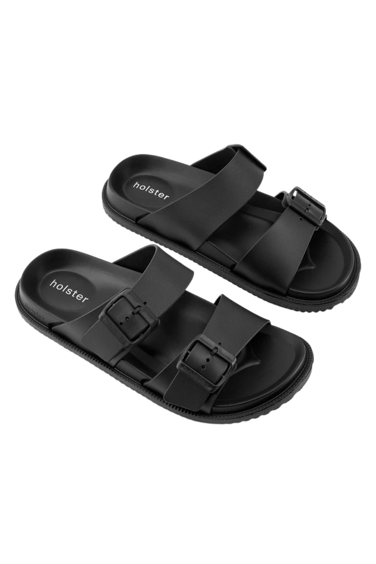 The Holster Soleseeker is a pair of black slip-on sandals with two adjustable buckle straps per shoe, a contoured footbed for arch support, and a textured sole. "Holster" is printed on the insole.