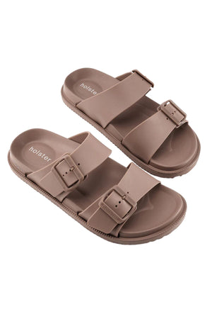 The Holster Soleseeker sandals are taupe vegan slides with two adjustable buckle straps per shoe, a contoured footbed for arch support, textured soles, and "holster" branding on the insole.