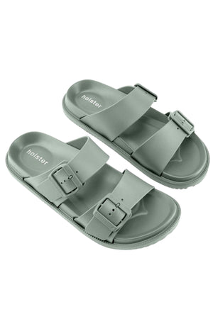 Holster Soleseeker: Light green vegan slide sandals with two adjustable buckle straps, textured soles, and "holster" branding on the footbeds, shown on a white background.